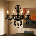 A closer view of the Clérachic chandelier's black glass arms lit above a dark dining table, an abstract painting behind.
