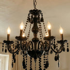 A close angle on the Clérachic chandelier's six lit candle arms and smoked glass column, set against a plaster ceiling.
