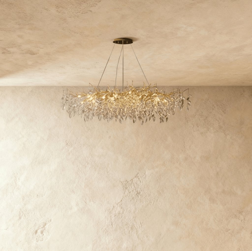 Clérachic crystal chandelier with a wide gold branch frame, its faceted leaves catching light near a plaster wall.