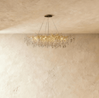 Clérachic crystal chandelier with a wide gold branch frame, its faceted leaves catching light near a plaster wall.