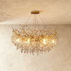 Clérachic gold chandelier shown close, its branch arms and cut crystal leaves glowing warm from within.