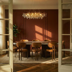 Clérachic gold branch chandelier lit above a dining table, its crystal leaves catching afternoon light on terracotta walls.