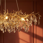 Clérachic chandelier detail showing gold branch arms hung with faceted crystal drops against a terracotta wall.
