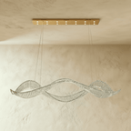 Clérachic twisting crystal ribbon chandelier on a gold rectangular ceiling plate, hung from fine cables above a limewash wall.