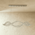 Clérachic twisting crystal chandelier with a polished chrome ceiling plate and fine suspension cables against a plaster wall.