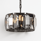 Clérachic black-framed drum chandelier lit warm, filament bulbs glowing through large smoky bevelled crystal panes on a chain.