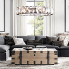 Clérachic wide ring chandelier of faceted crystal hanging above a charcoal sofa and wooden trunk table by a tall window.