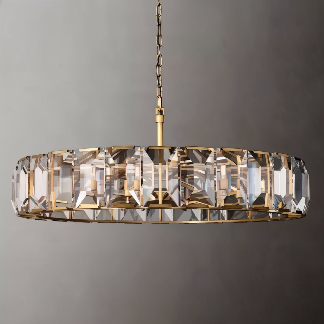 Clérachic large brass ring chandelier of clear faceted crystal panes with a brass rod and chain on a grey backdrop.