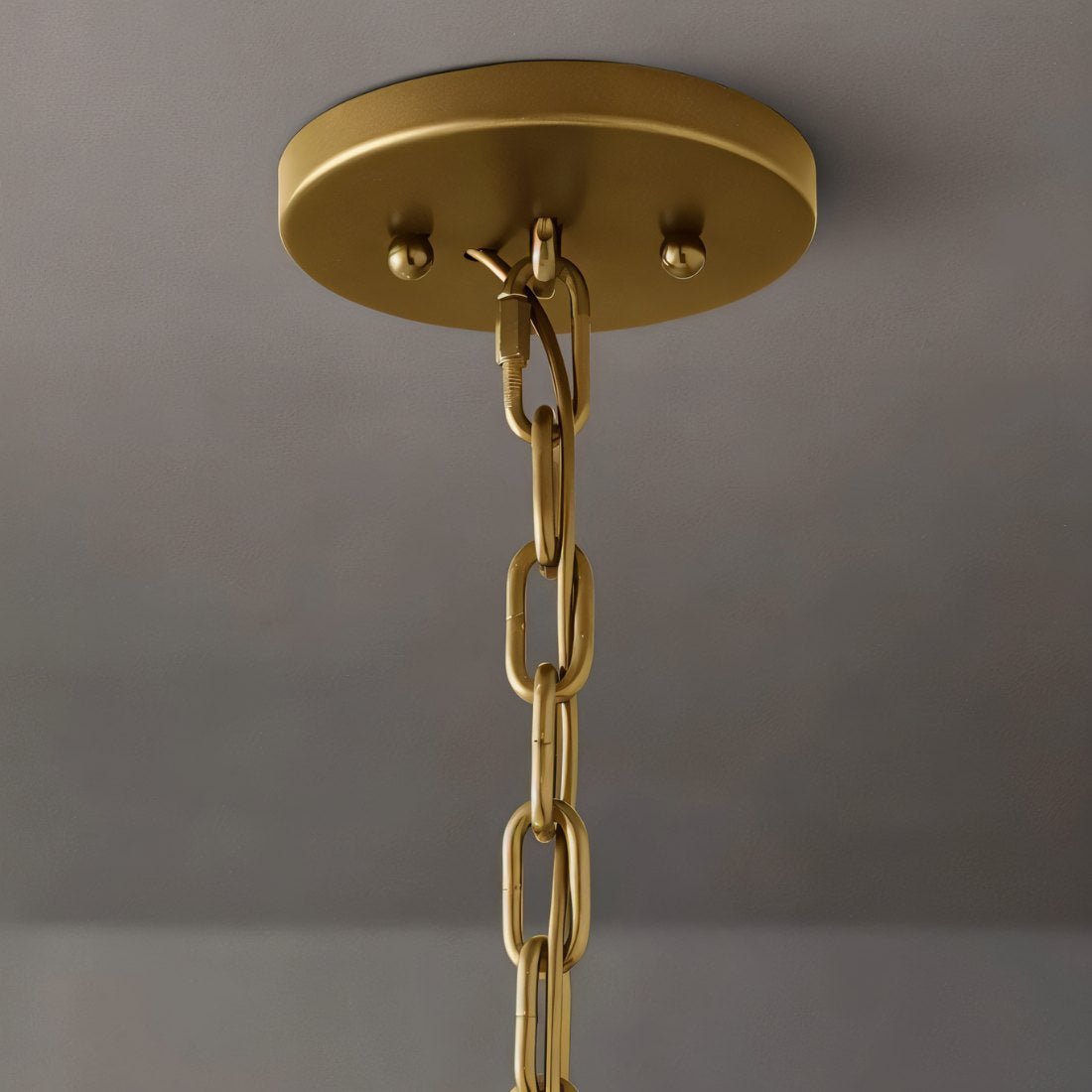 Clérachic brass ceiling canopy with two ball finials and a chain link, seen from below against a grey wall.