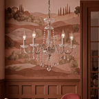 Clérachic candle-arm chandelier with clear crystal drops, lit in a room with a pastoral hills mural and wood wall panelling.