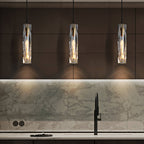 Three Clérachic crystal pendants in a row above a kitchen worktop, in front of a marble splashback and a black tap.