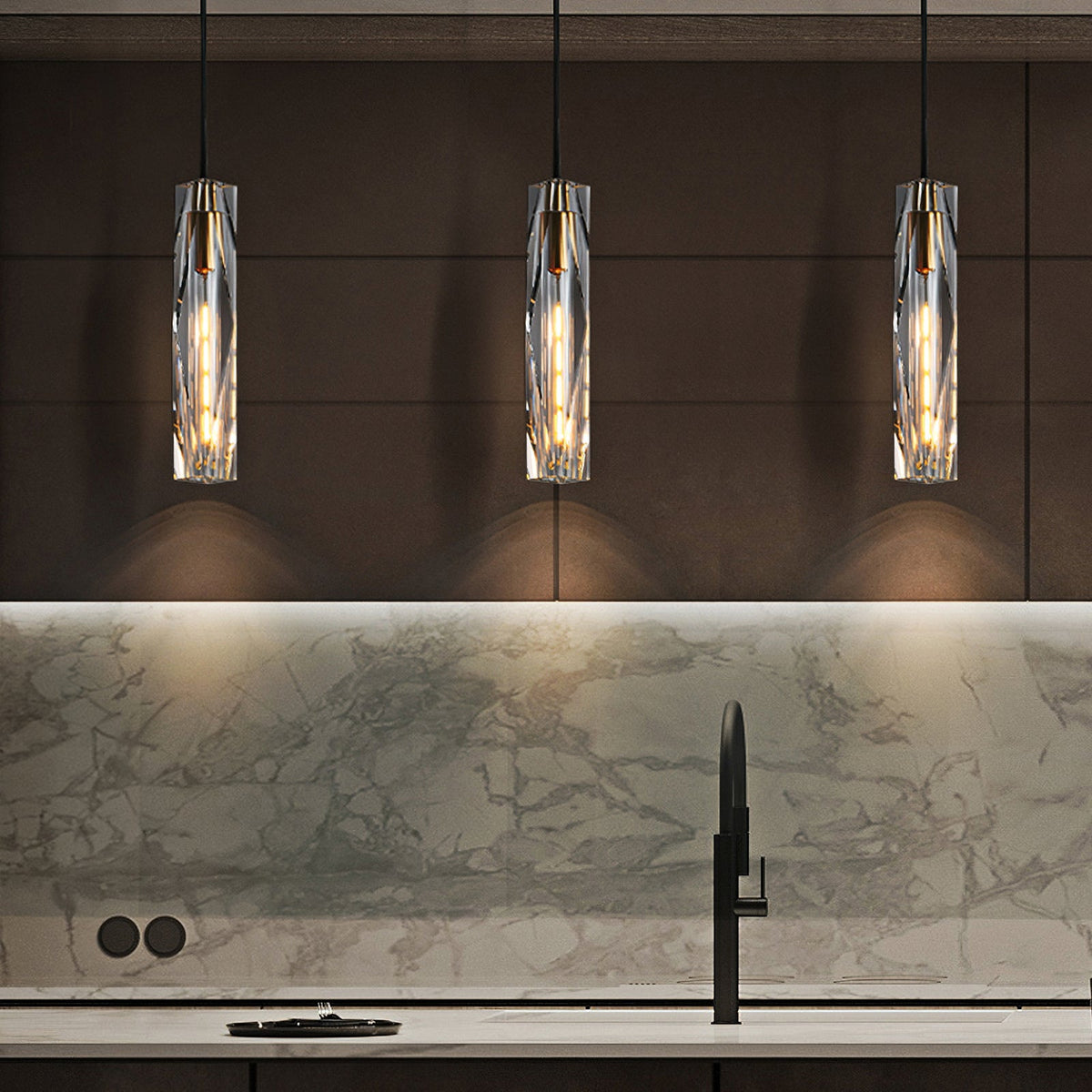 Three Clérachic crystal pendants in a row above a kitchen worktop, in front of a marble splashback and a black tap.