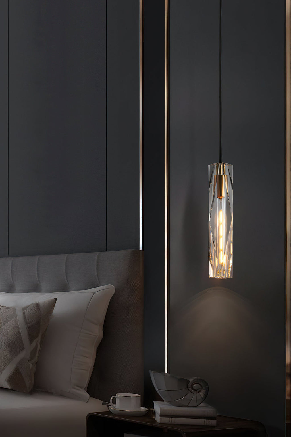 Clérachic crystal pendant beside a grey upholstered bed, with a cup and a shell ornament on the bedside table below.