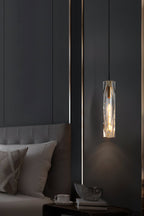 Clérachic crystal pendant beside a grey upholstered bed, with a cup and a shell ornament on the bedside table below.