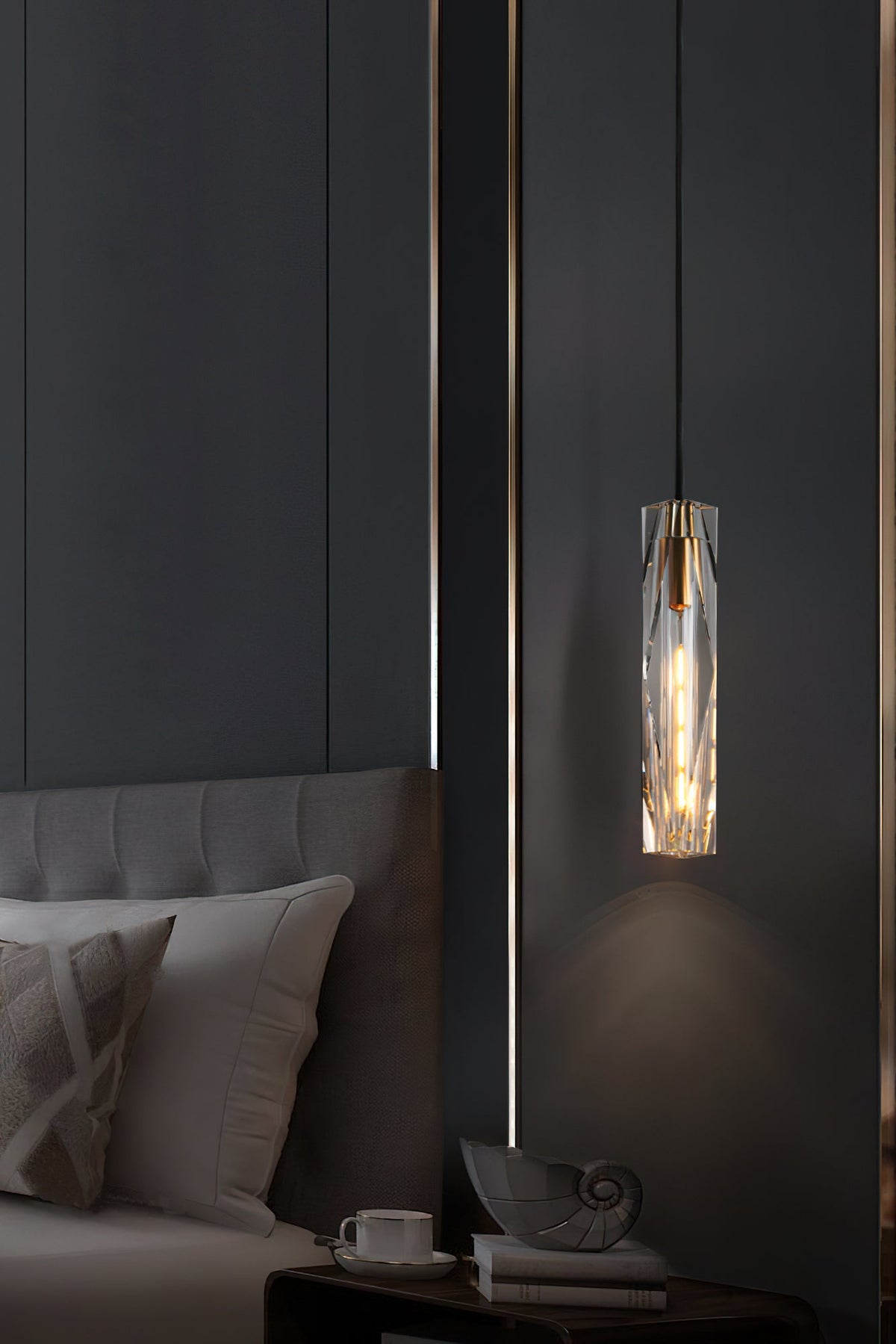 Clérachic crystal pendant beside a grey upholstered bed, with a cup and a shell ornament on the bedside table below.