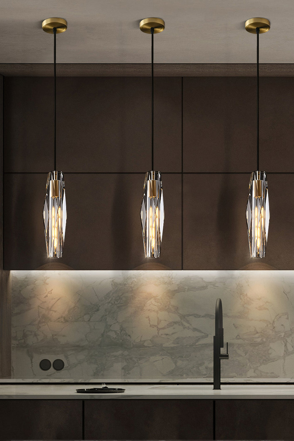 Three Clérachic crystal pendants with brass-toned ceiling plates, hung over a kitchen counter with a marble splashback.