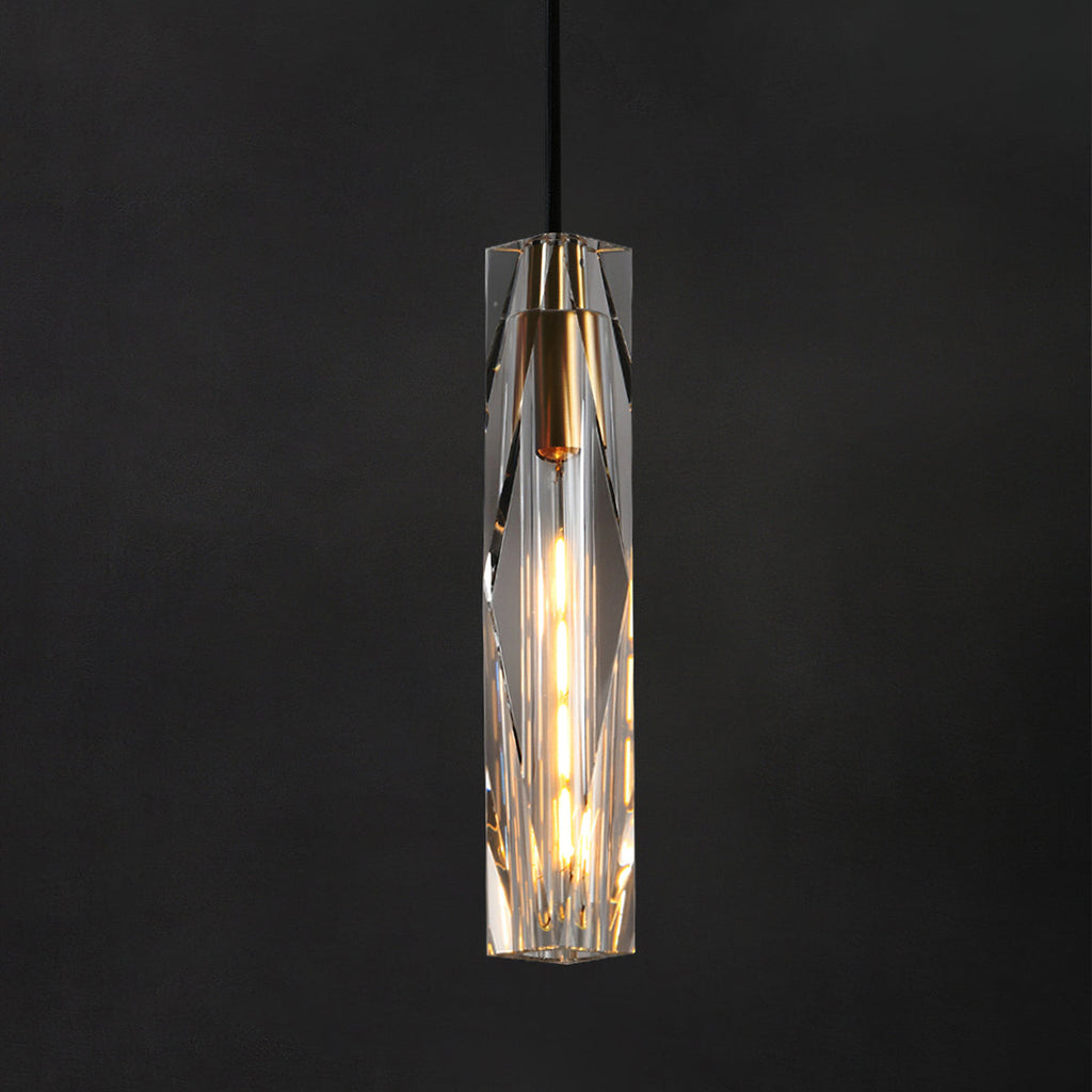 Clérachic crystal pendant in front of a charcoal backdrop, with the filament bulb glowing through the faceted glass.