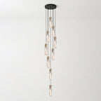 Tall cascade of Clérachic crystal pendants hanging at varied heights from a round black ceiling plate, against a pale wall.