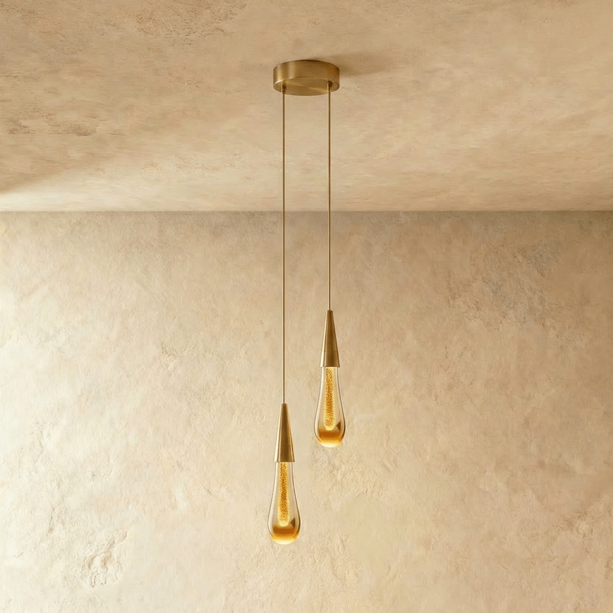 Clérachic crystal drop pendant light shown as a pair, two amber glass teardrops on brass stems against a plaster ceiling.