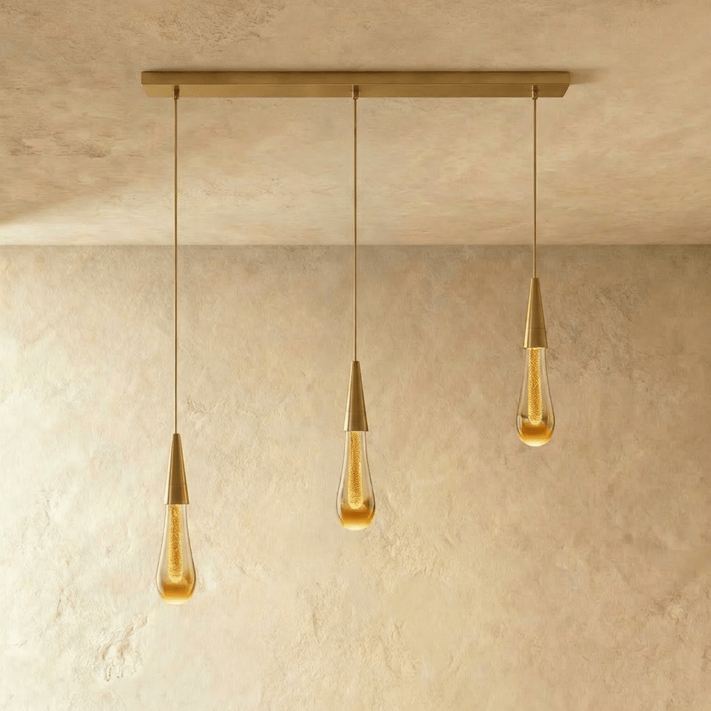 Clérachic crystal drop pendant light in a three-piece linear row, amber glass teardrops hung from a slim brass bar.
