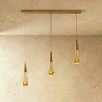 Clérachic crystal drop pendant light in a three-piece linear row, amber glass teardrops hung from a slim brass bar.
