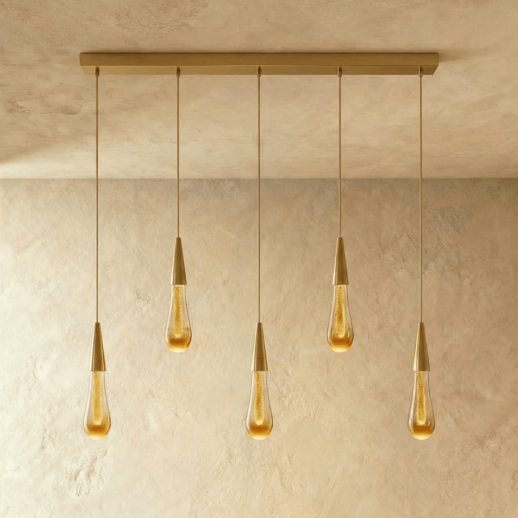 Clérachic crystal drop pendant light in a five-piece linear row, amber glass teardrops evenly spaced along a brass bar.