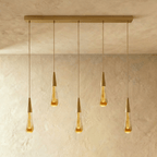 Clérachic crystal drop pendant light in a five-piece linear row, amber glass teardrops evenly spaced along a brass bar.