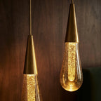 Close-up of two lit Clérachic crystal drop pendants, their bubbled amber glass glowing against dark wood panelling.