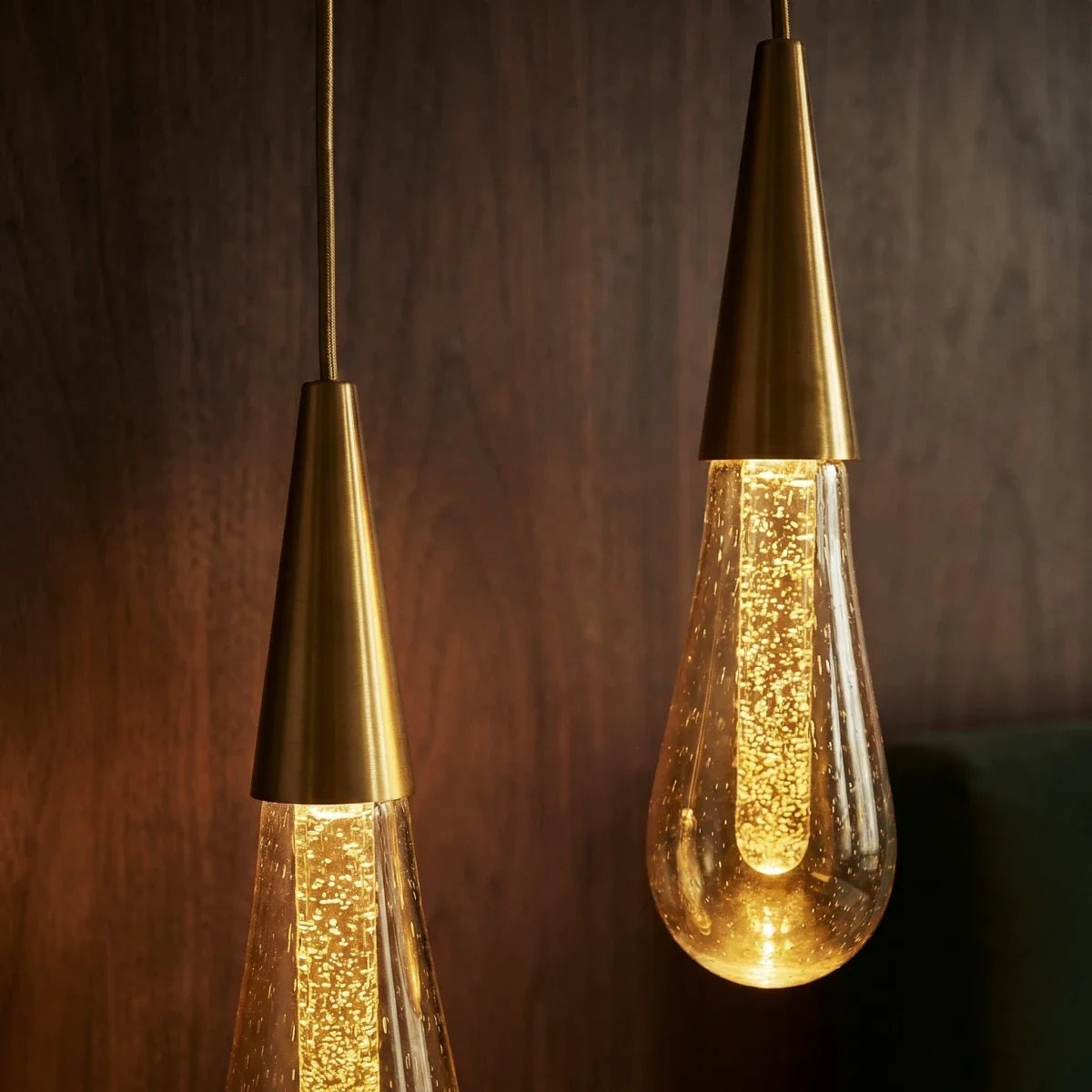 Close-up of two lit Clérachic crystal drop pendants, their bubbled amber glass glowing against dark wood panelling.