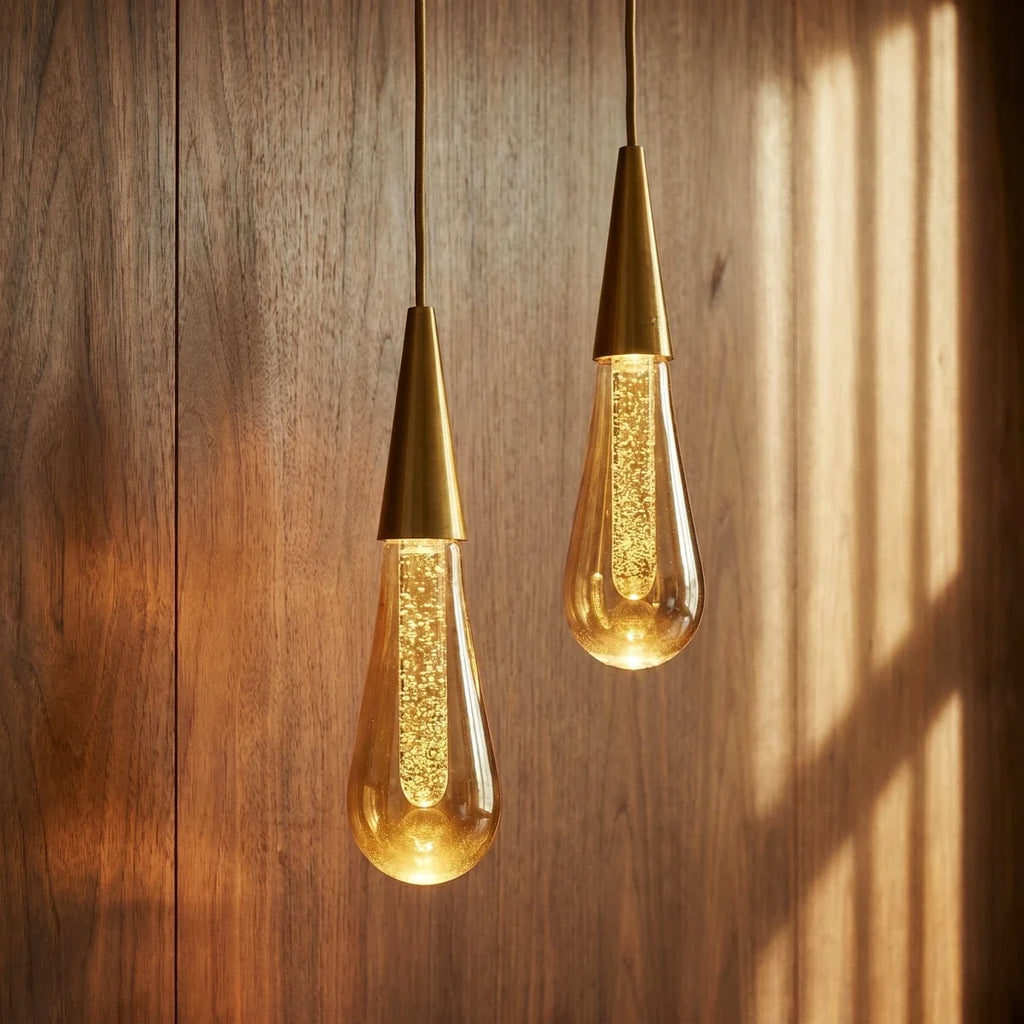 Close-up of two lit Clérachic crystal drop pendants catching afternoon light against a warm wood-panelled wall.