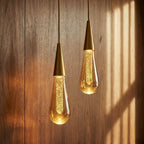 Close-up of two lit Clérachic crystal drop pendants catching afternoon light against a warm wood-panelled wall.