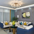 Lit gold crystal-flower ceiling light from Clérachic above a living room with navy leather sofas, a gold-trimmed grey wall and teal curtains.