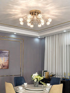 Lit crystal-flower ceiling light from Clérachic with a gold frame, above a round dining table in a room with grey walls and sheer curtains.