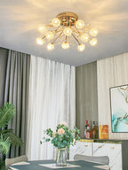 Gold ceiling light from Clérachic with glass flower shades lit above a dining table with a bouquet, in front of grey and white curtains.