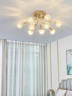 Gold flower-shade ceiling light from Clérachic glowing near a window with sheer green-grey curtains and an upholstered chair.
