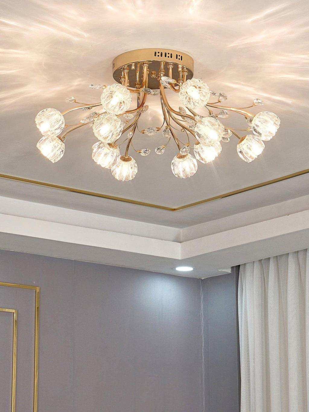 Lit gold flower-shade ceiling light from Clérachic below a recessed ceiling with a thin gold trim, beside a grey wall and curtains.