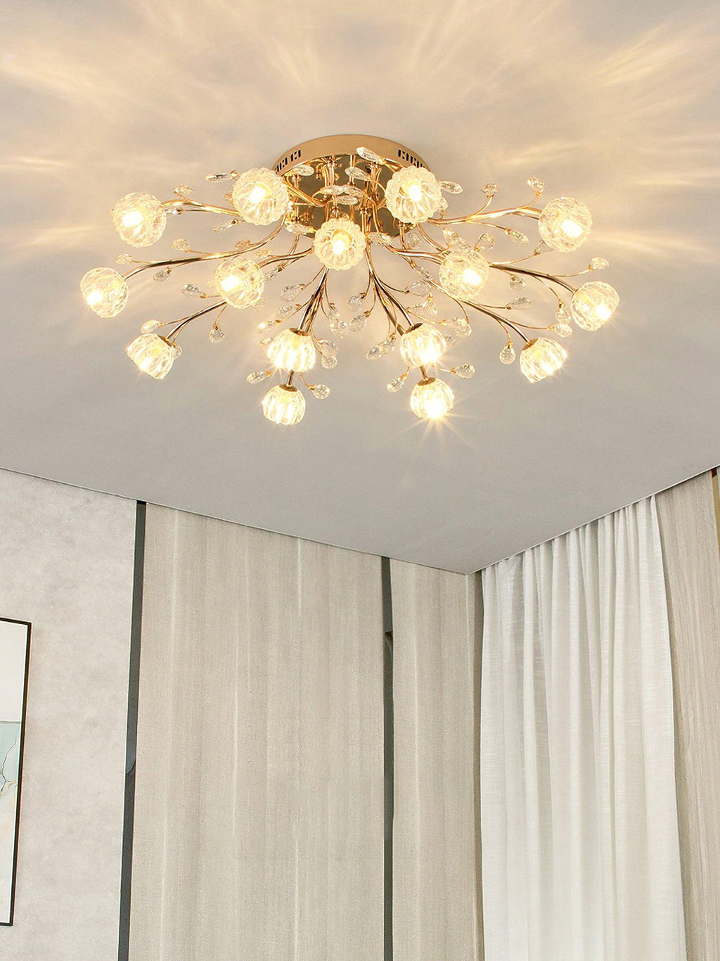 Gold branching ceiling light from Clérachic with many clear flower shades, glowing in a corner with pale curtains.