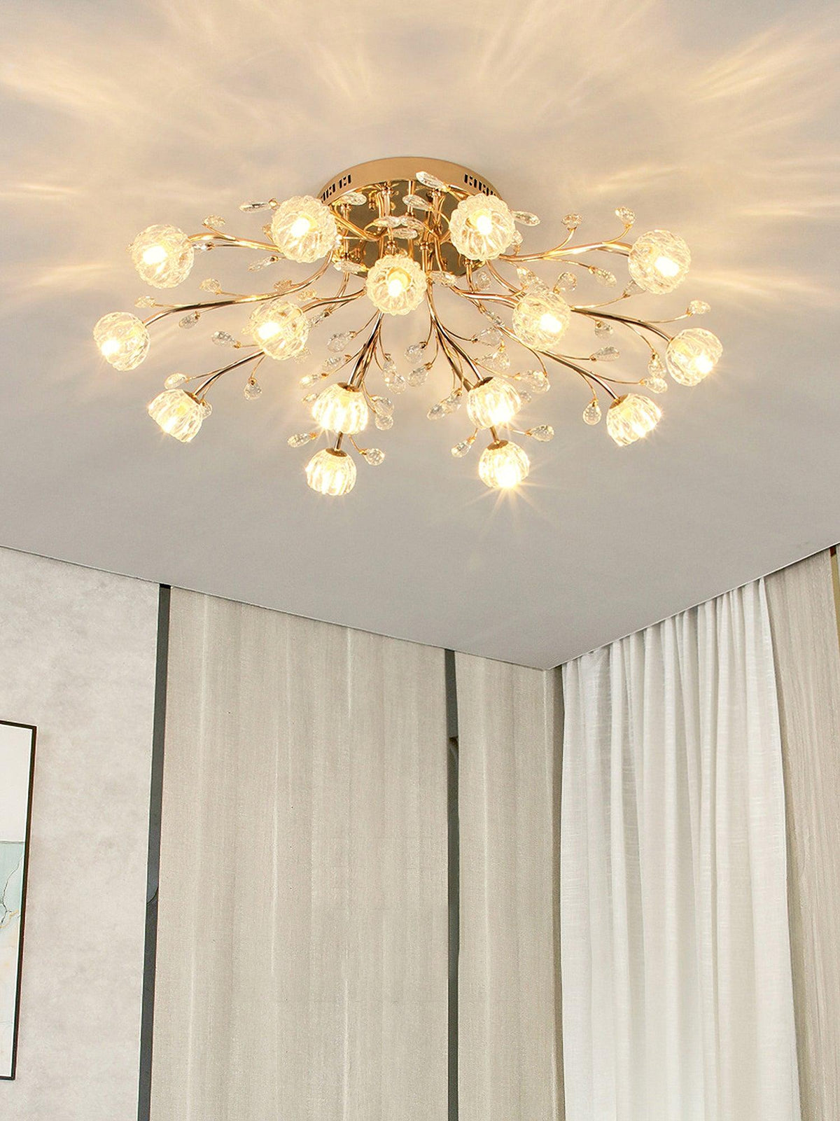Gold branching ceiling light from Clérachic with many clear flower shades, glowing in a corner with pale curtains.