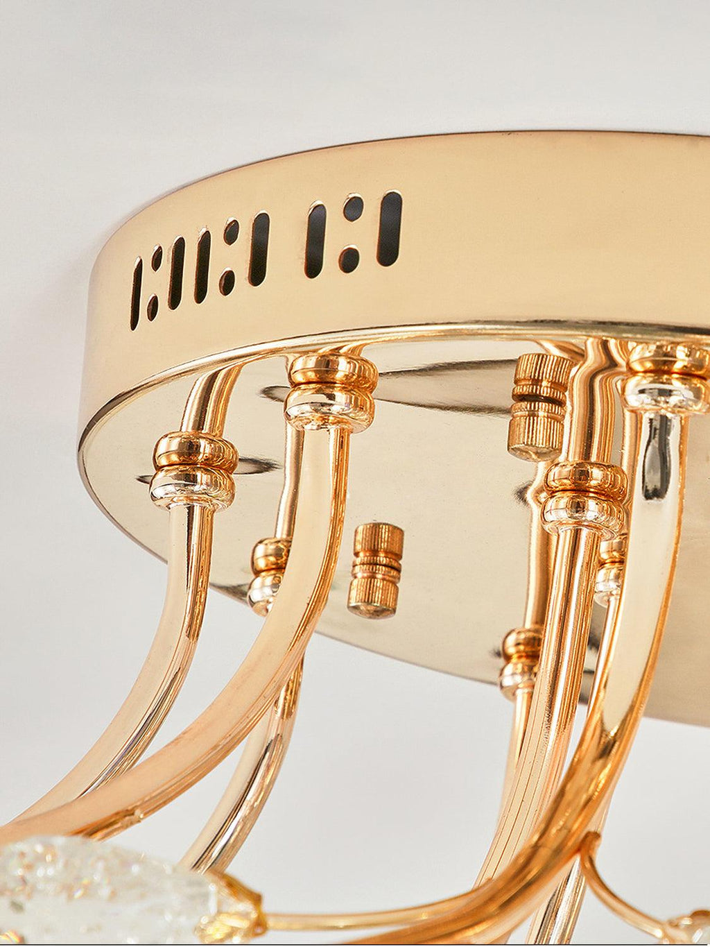 Close view of the gold round canopy of this Clérachic ceiling light, with vent slots and curved stems leaving its underside.