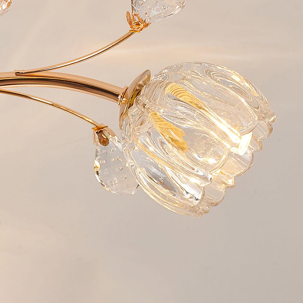Close view of a clear glass flower shade on a gold stem of this Clérachic ceiling light, with a crystal leaf beside it.