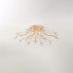 Unlit gold flush ceiling light from Clérachic with clear glass flower shades and crystal leaves, on a pale ceiling.