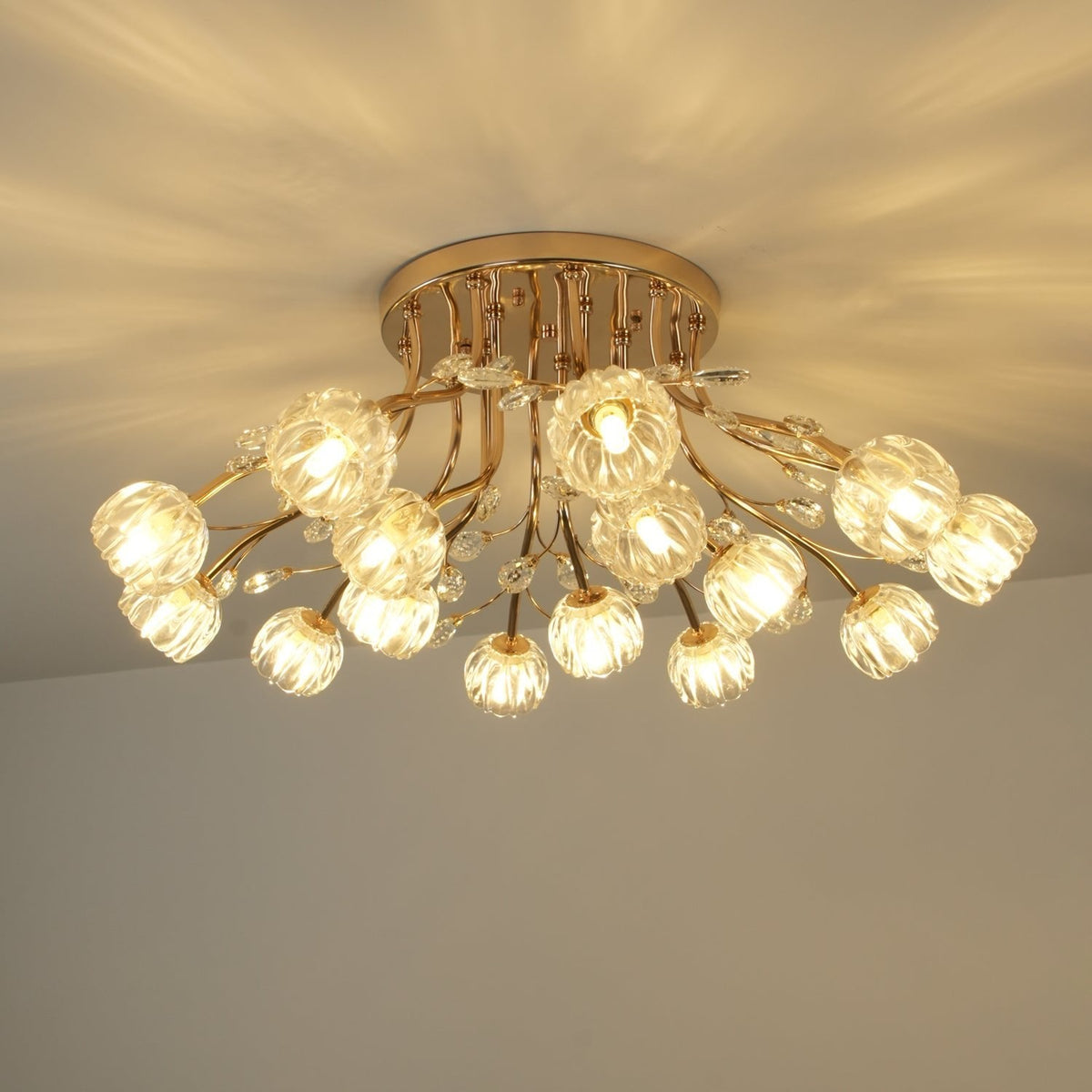 Side view of a lit gold Clérachic ceiling light with a dozen ribbed glass flower shades and a round gold canopy.
