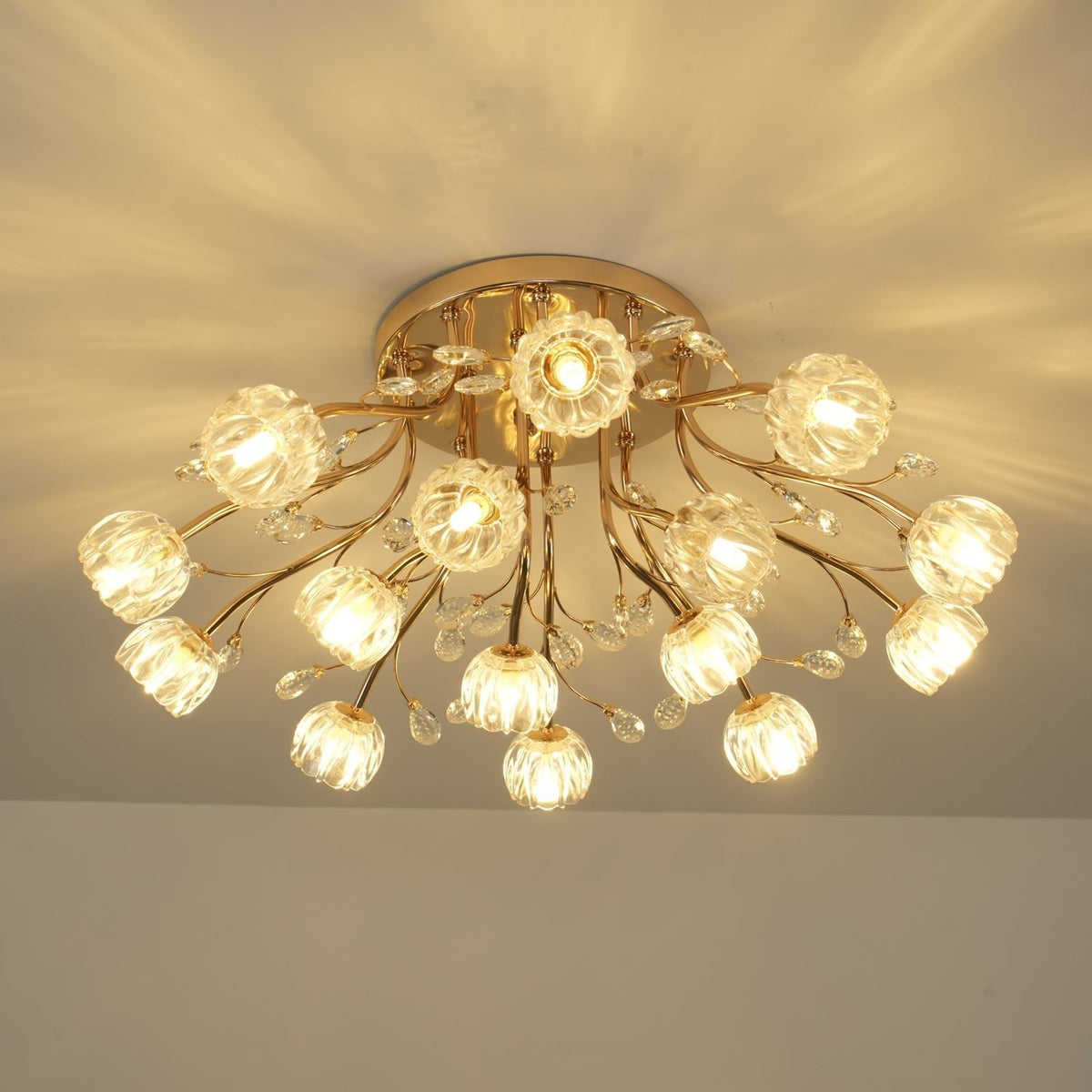 Lit gold ceiling light from Clérachic with ribbed glass flower shades, crystal drops and a warm patterned glow overhead.