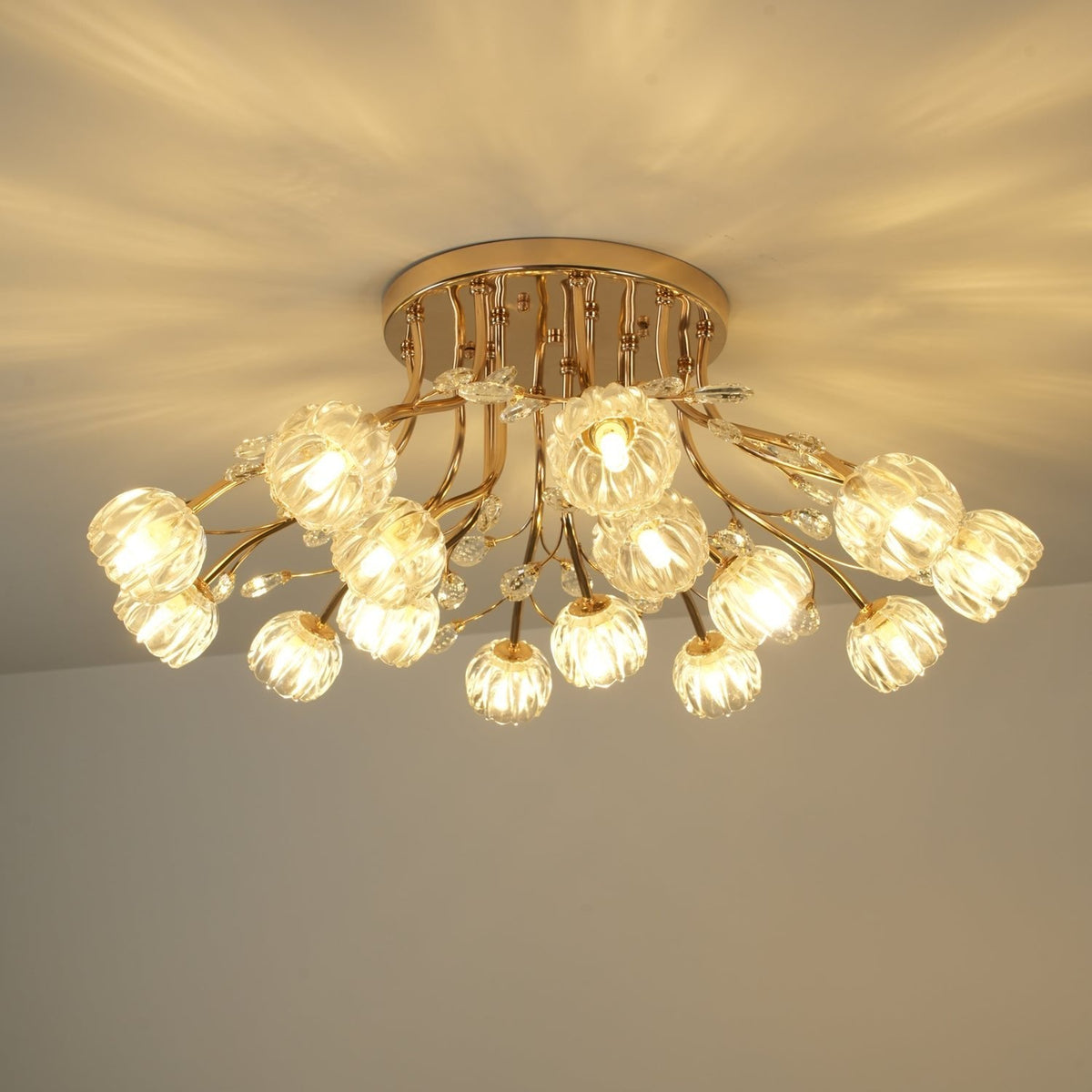 Lit Clérachic ceiling light with a gold canopy and ribbed glass flower shades, the stems curving down from the ceiling.