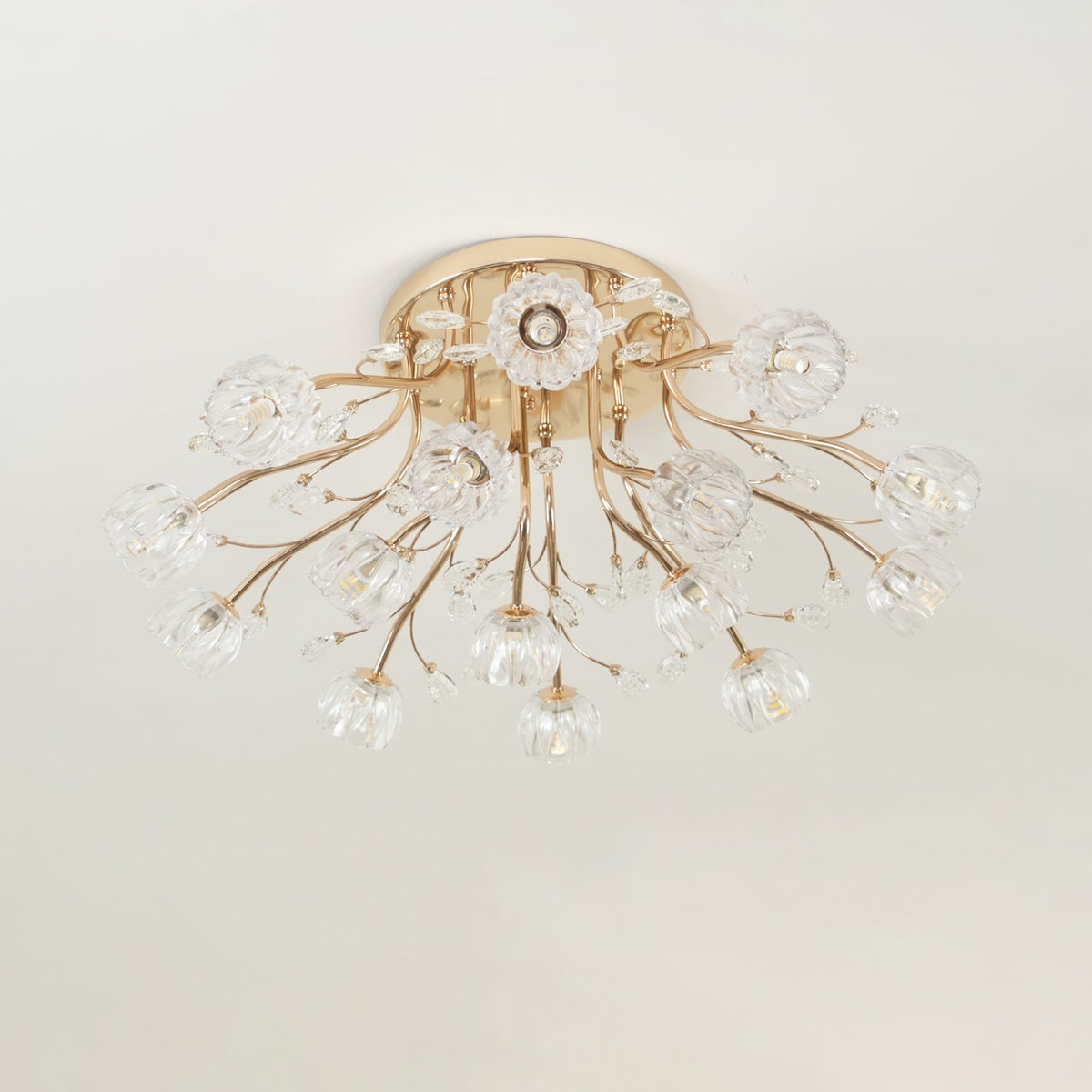 Unlit gold ceiling light from Clérachic with clear glass flower shades and fine crystal leaves on slender stems.