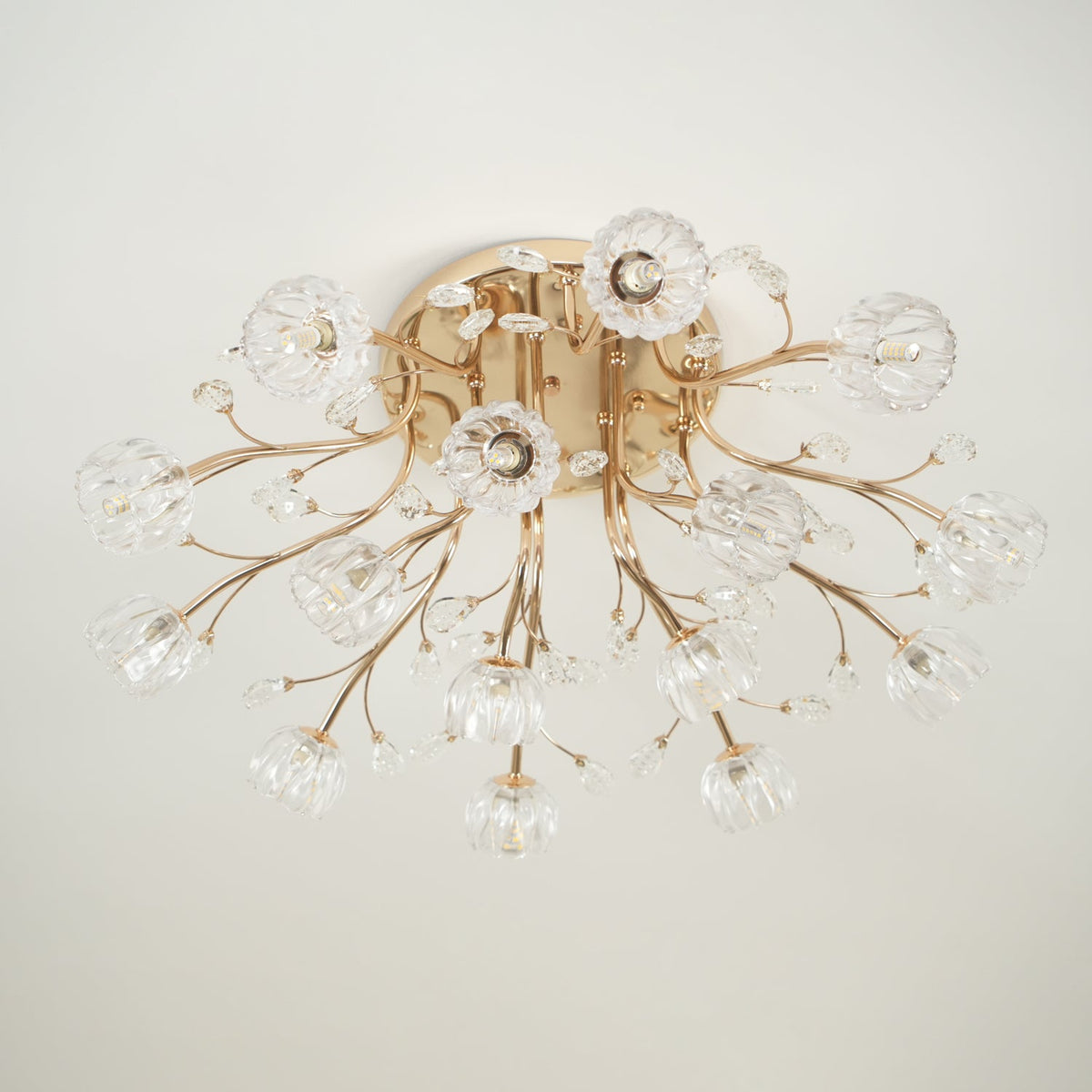 Gold flower-shade ceiling light from Clérachic, unlit, with crystal leaves and a few bulbs visible through the clear glass.
