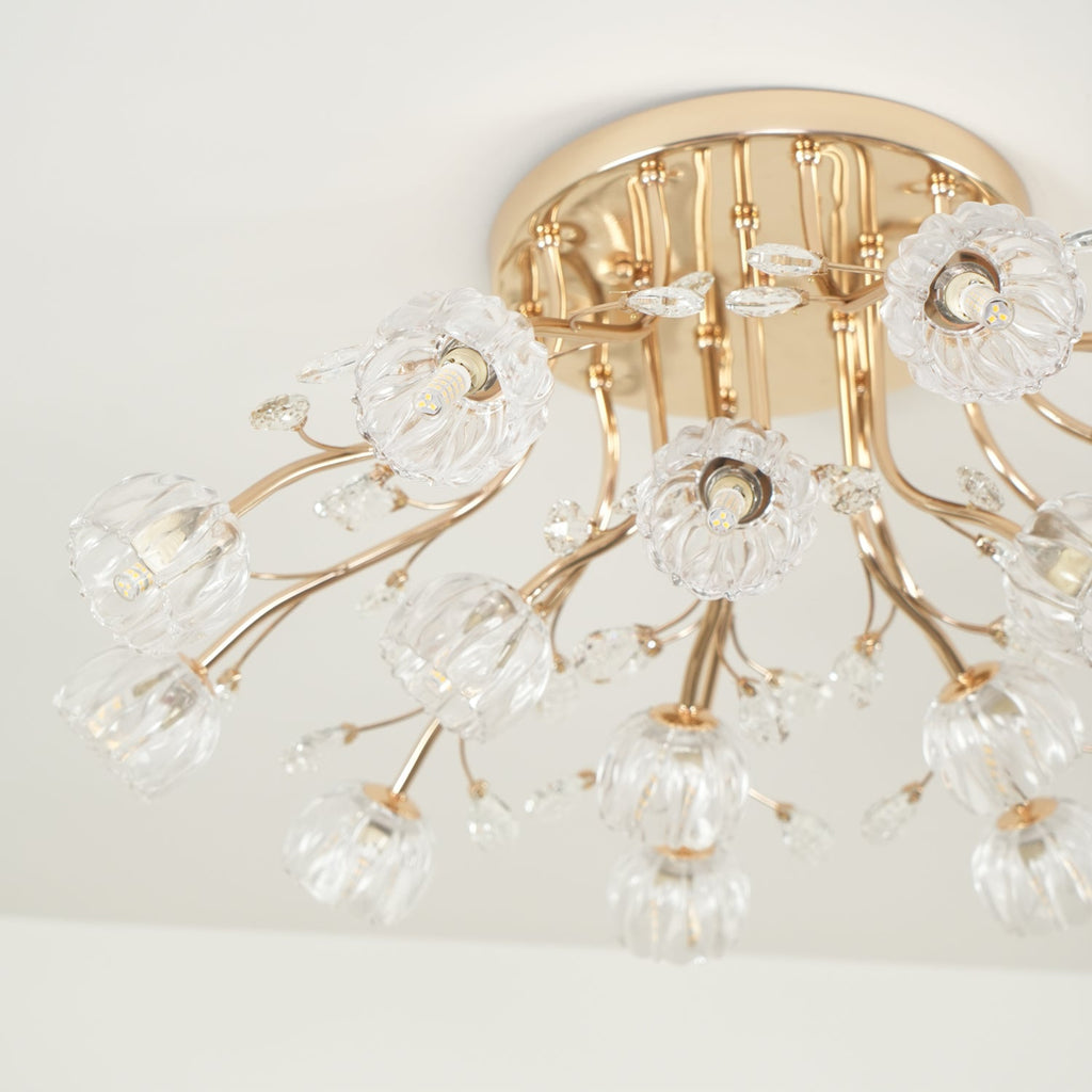 Close view of a gold canopy, curved stems and clear glass flower shades on this Clérachic ceiling light, unlit.
