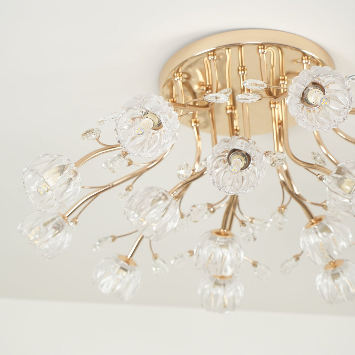 Close view of a gold canopy, curved stems and clear glass flower shades on this Clérachic ceiling light, unlit.