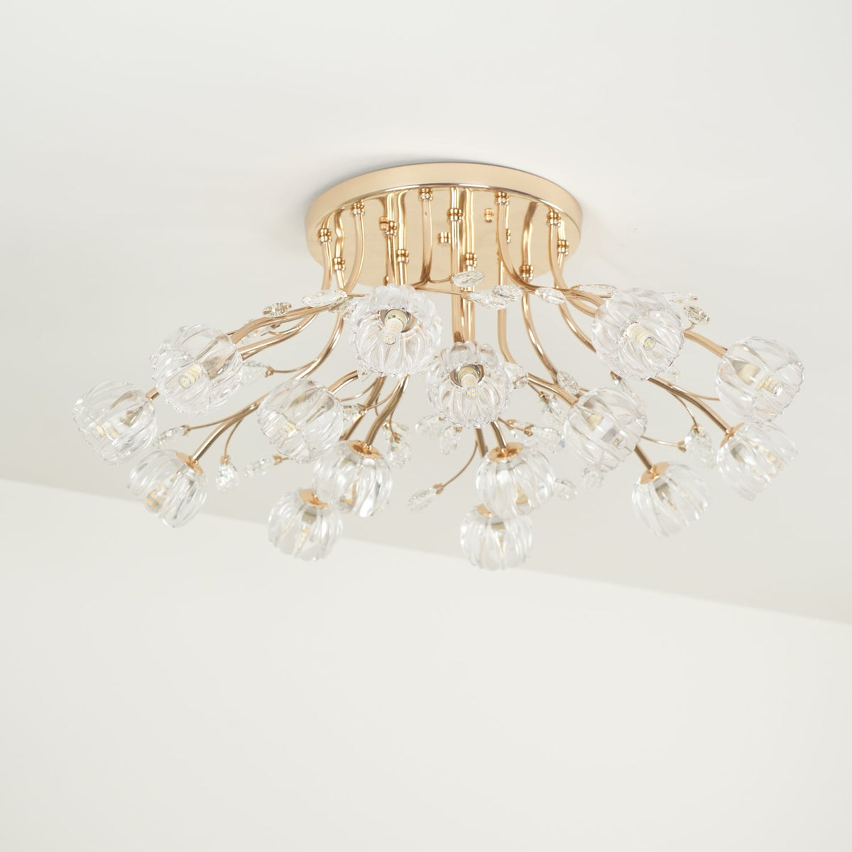 Side-on view of a gold flush ceiling light from Clérachic, with its stems fanning out and clear glass flowers below.