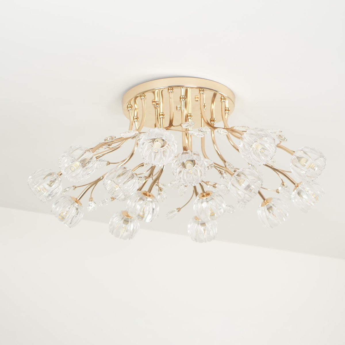 Unlit gold Clérachic ceiling light with a round canopy and a spread of clear glass flower shades, seen from the side.
